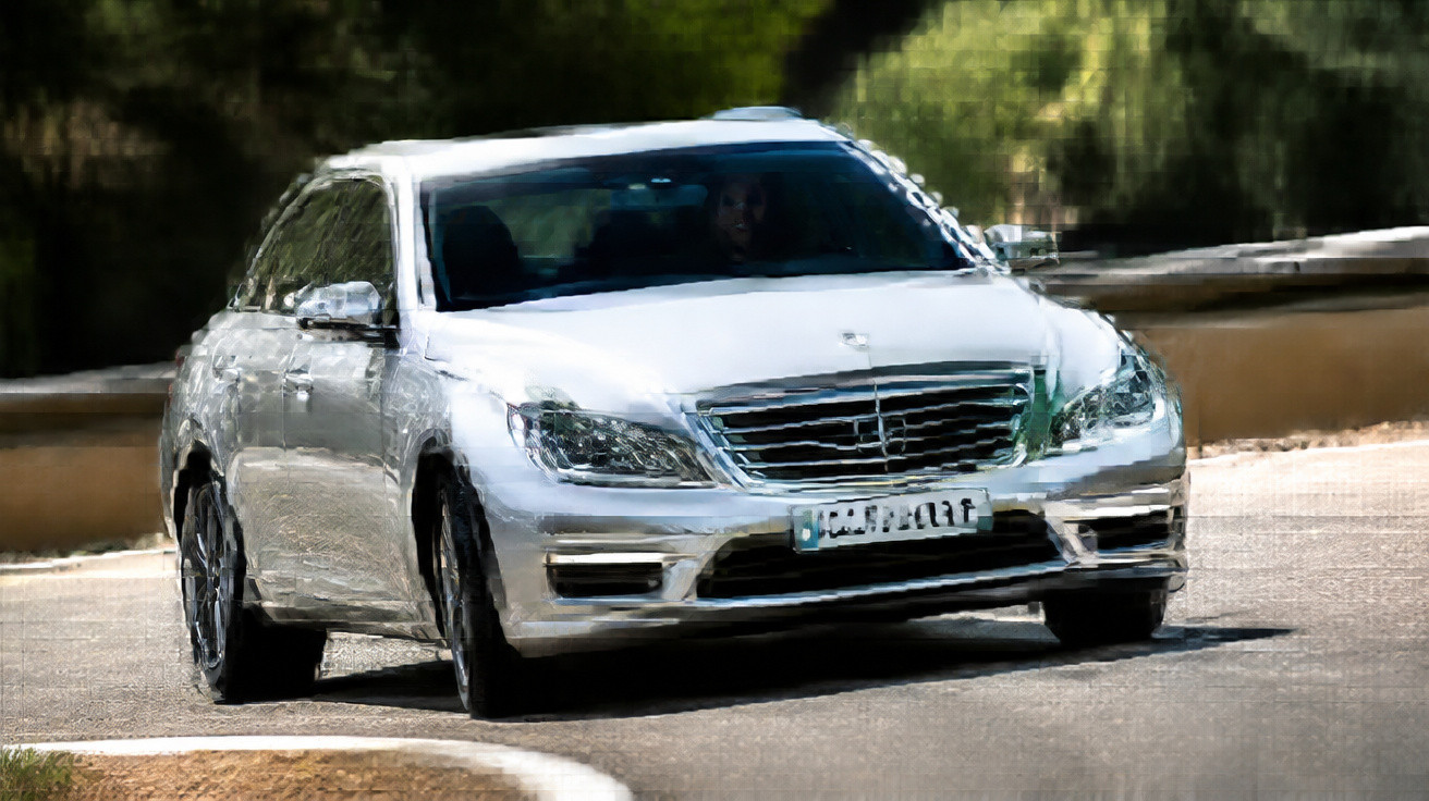 Carro prata sedan Mercedes-Benz em curva de estrada rodeada por vegetação verde.